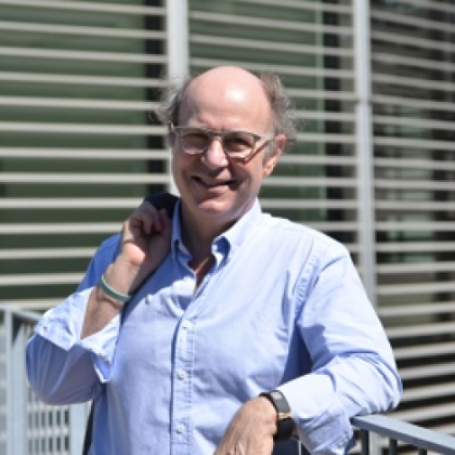 Picture of Frank Wilczek in a blue shirt standing in front of the AlbaNova building in Stockholm.
