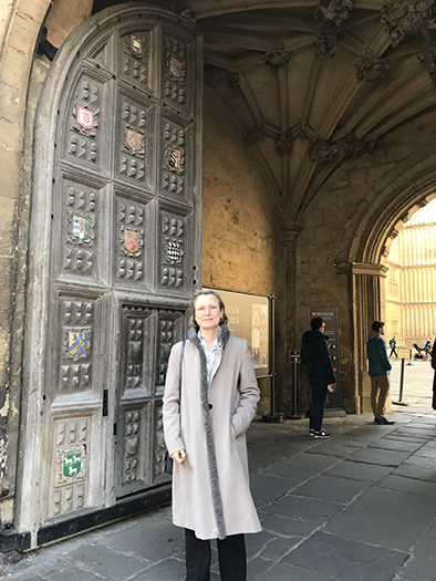 Maria Kuteeva standing outside a large gate at the University of Oxford.