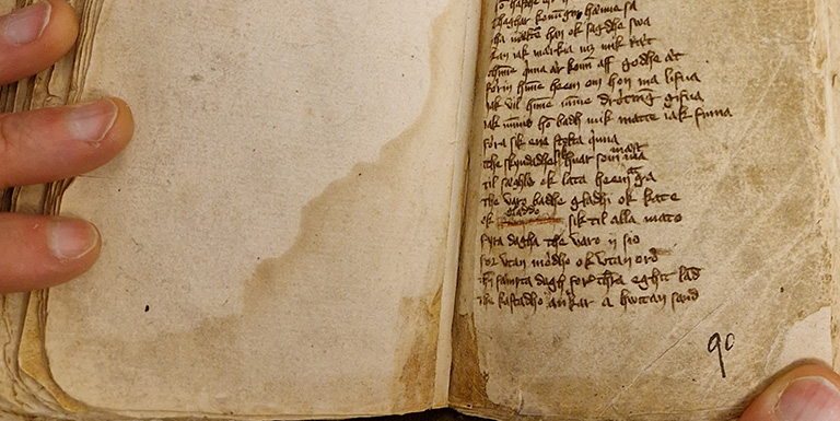 Smal uppslagen bok med liten handskriven text. Man ser fingertopparna på händer som håller i boken.