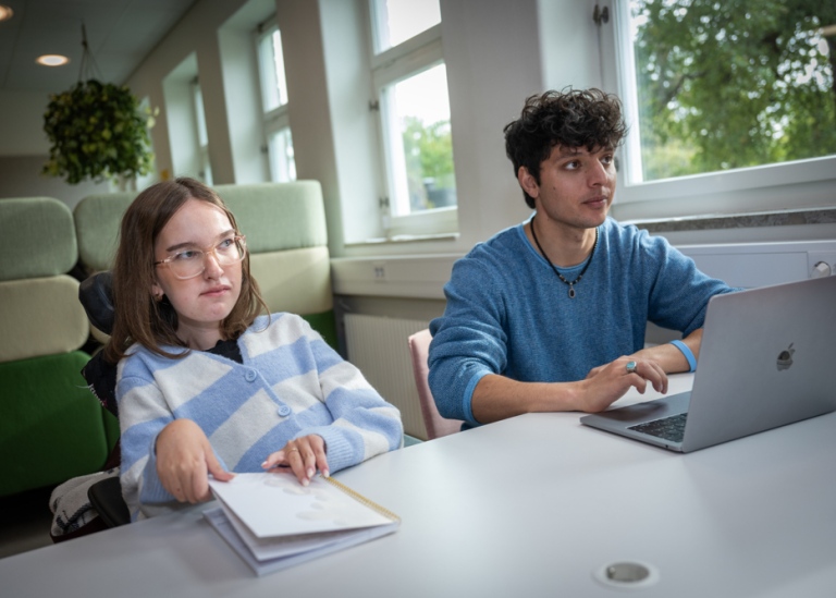 Två studenter sitter och studerar vid stort bord intill fönster på BUV.