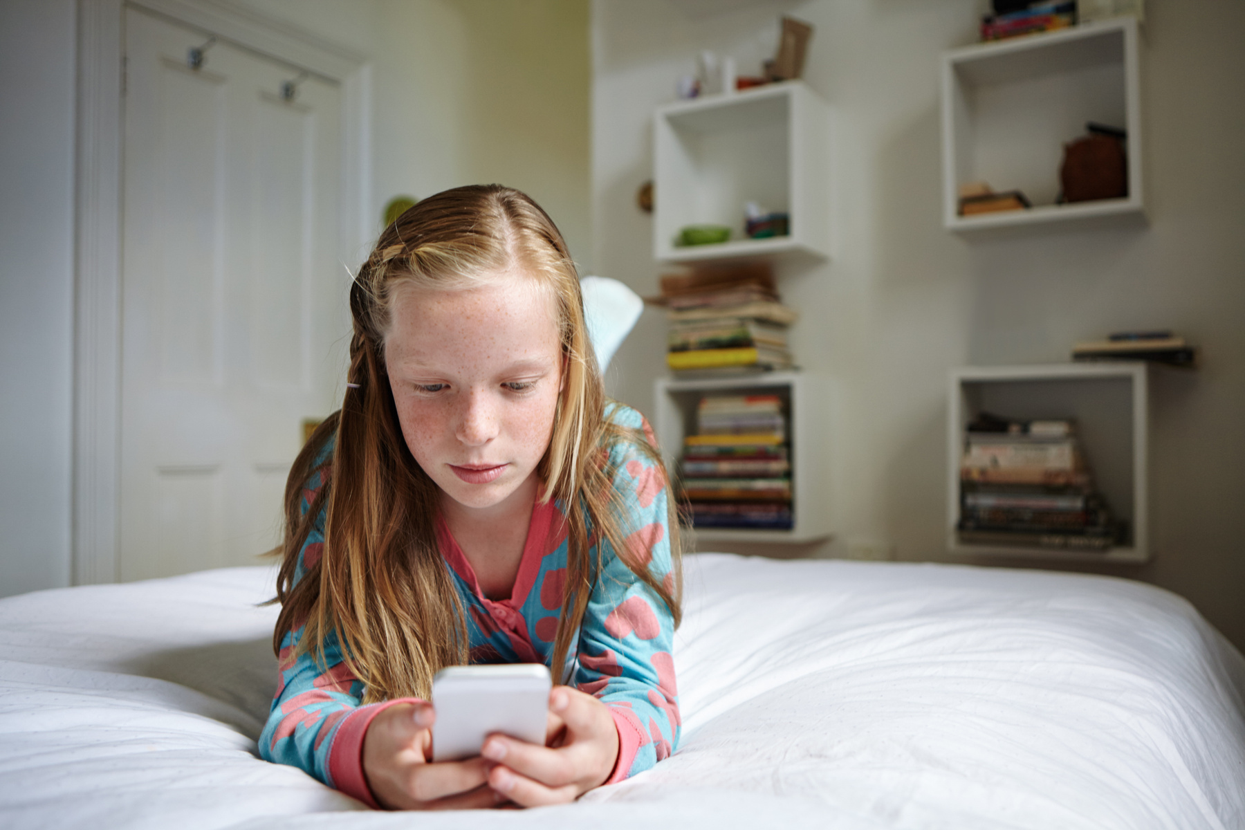 Flicka ligger på säng och tittar på en smartphone