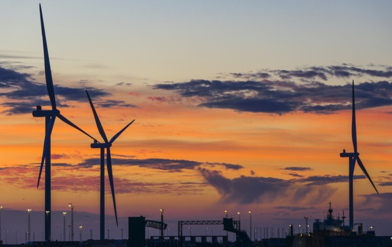 Windmills by city in sunset.