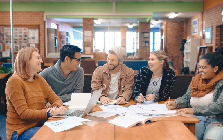A diverse group of five adults sitting around a wooden table in a library.