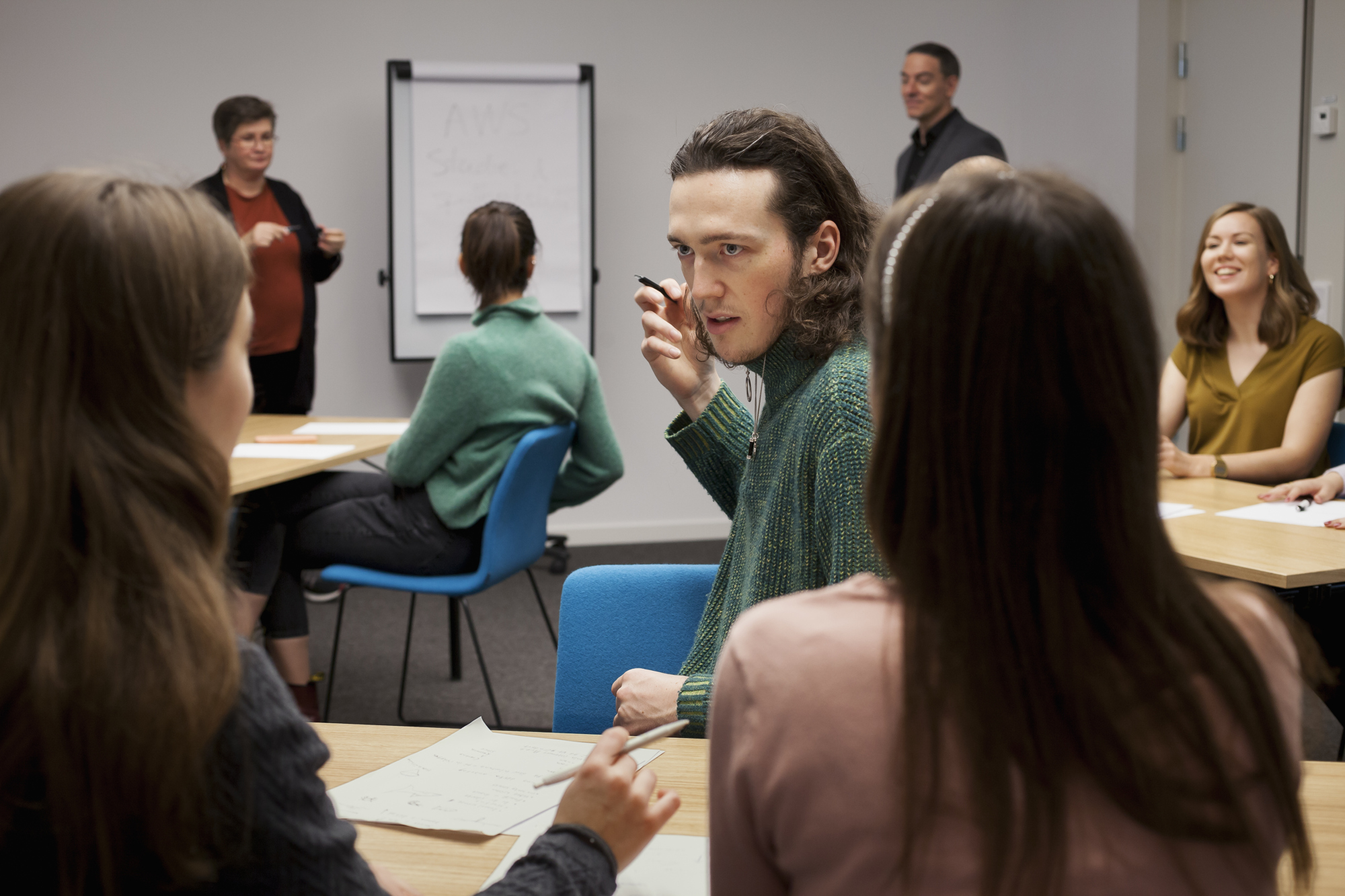 Sju personer diskuterar fritt i ett rum med ett blädderblock redo för anteckningar i bakgrunden.
