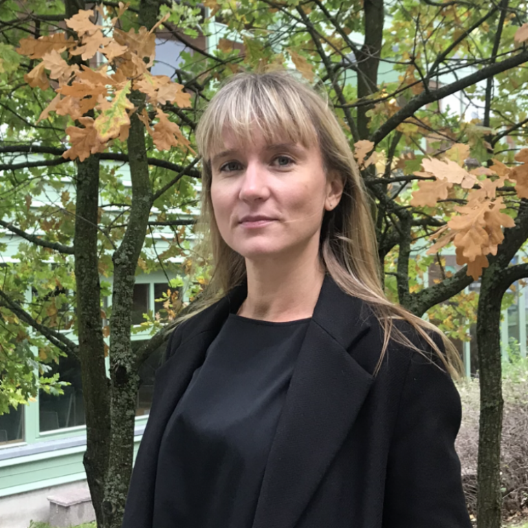 Frida Beckman står vid ett träd där några blad är orangea