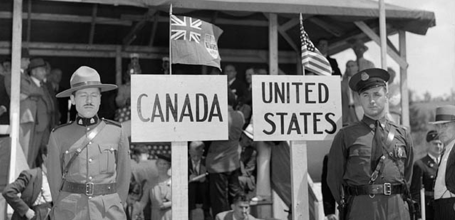 A Royal Canadian Mounted Police constable stands in front of a sign marked "Canada" while to his lef