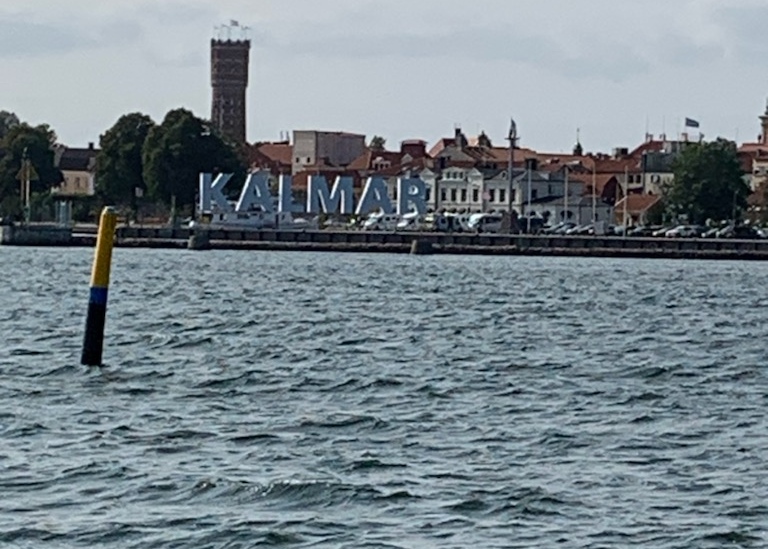 hav och stadsilhuett med texten "Kalmar" uppsatt vid kajkanten.