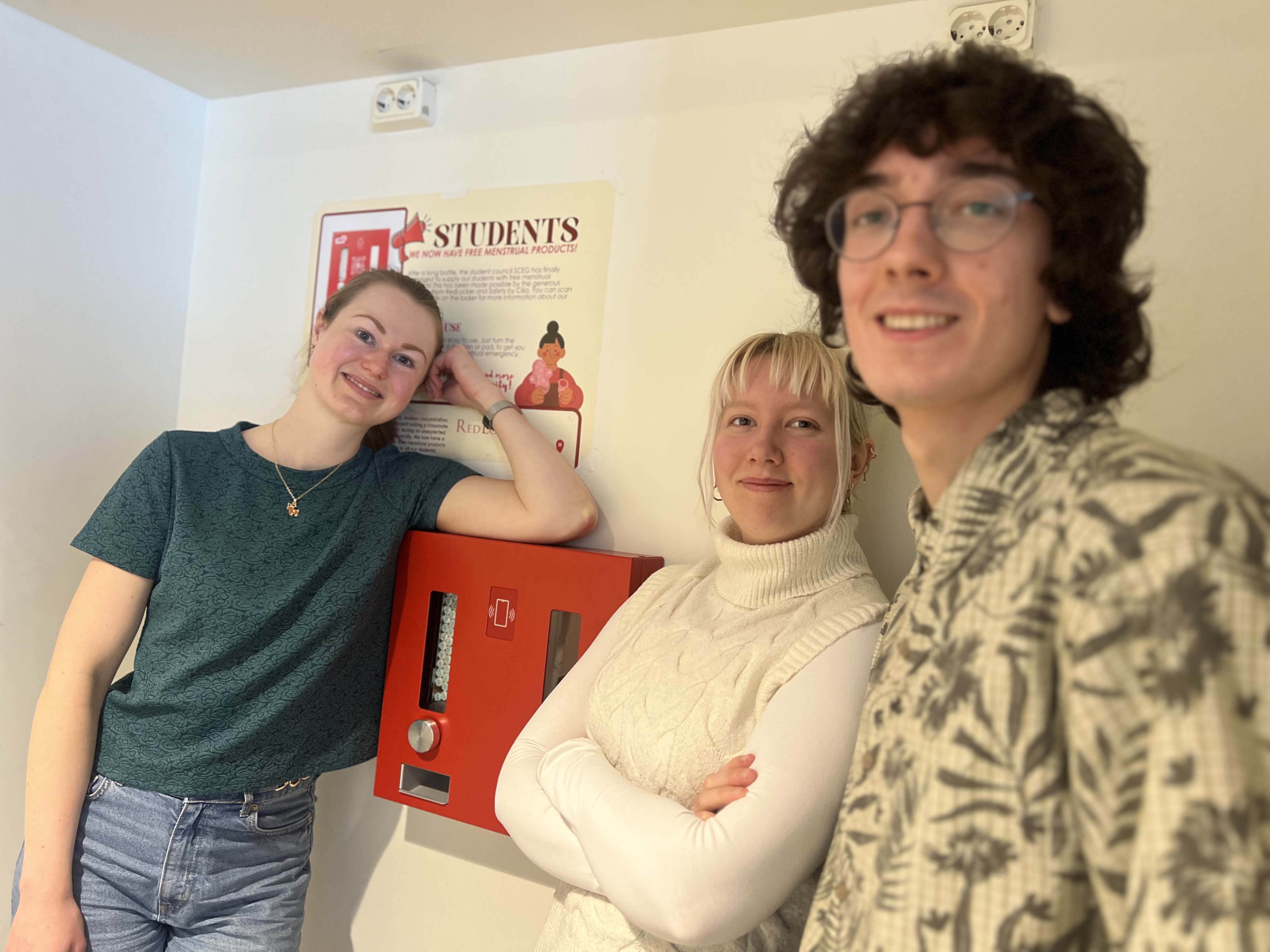 3 students leaning against a red locker on the wall