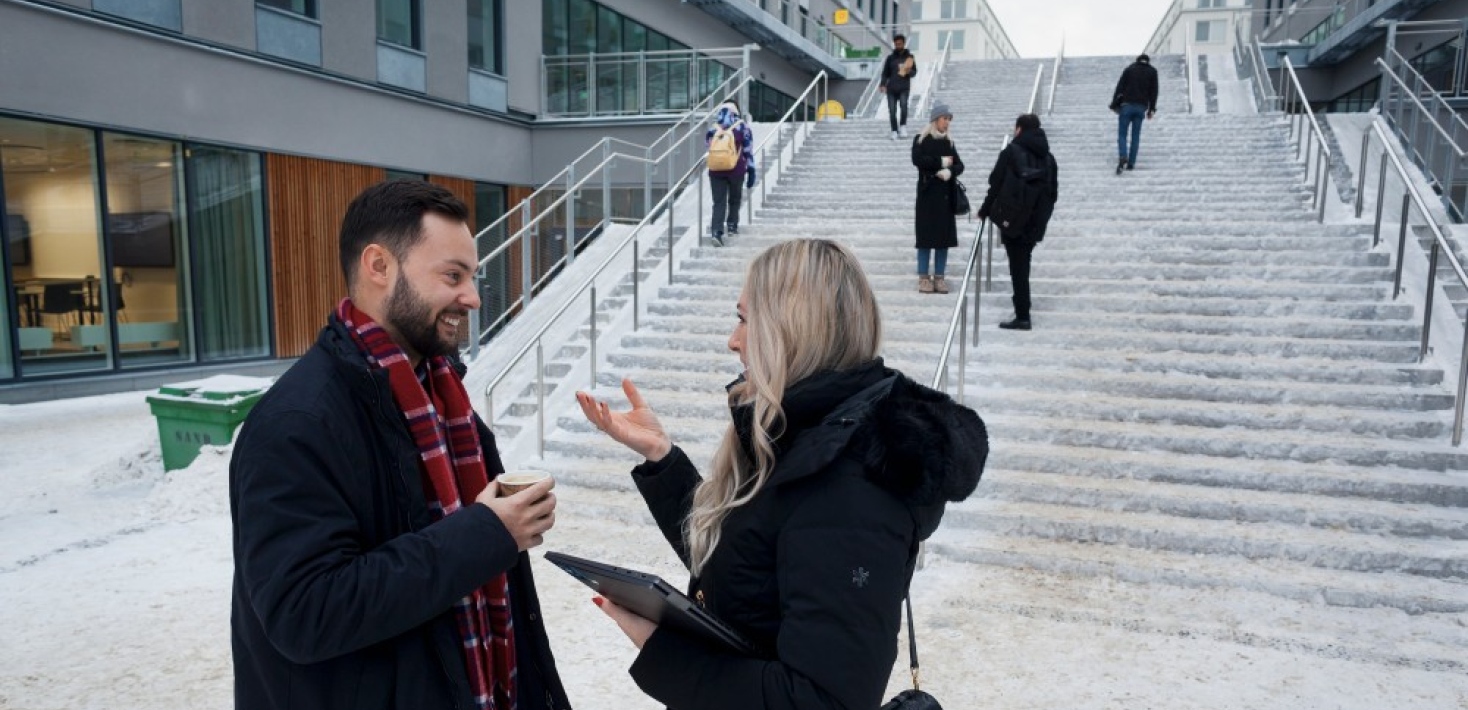 Campus Albano, där två personer pratar med varandra vid en trappa.