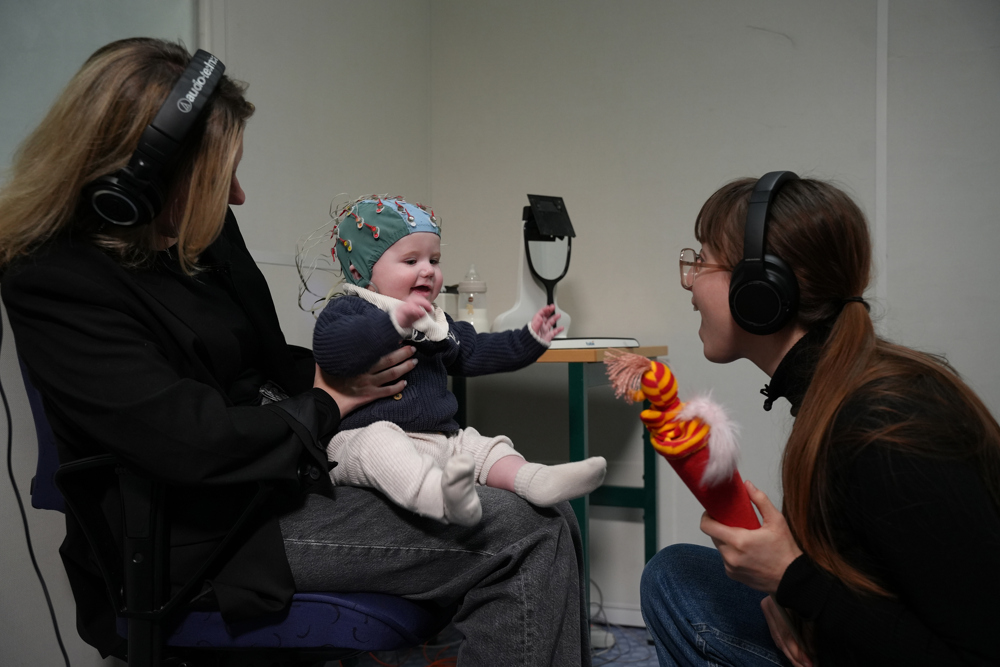 En baby har en huva på huvdet och interagerar med två personer.