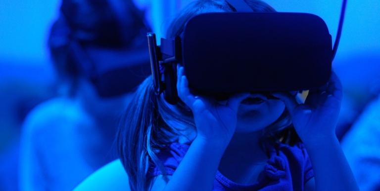Genrebild , blåtonad, på en liten flicka som testar VR-glasögon med en annan person i bakgrunden.