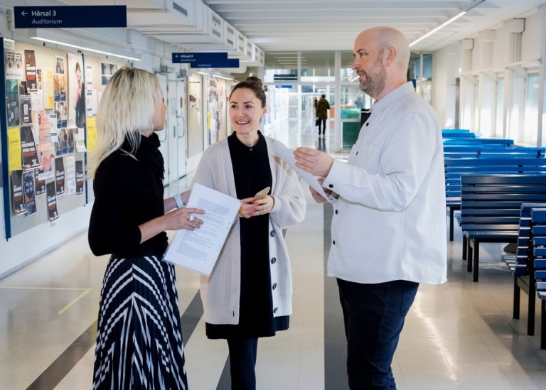 Två kvinnor och en man står och diskuterar i korriodor i Södra huset.
