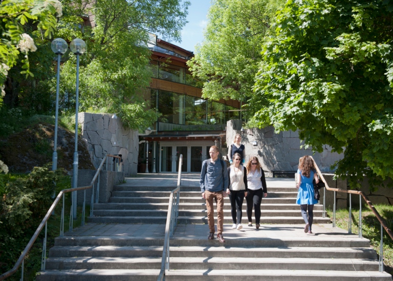 Folk går i trappan upp till Aula Magna som är inbäddad i grönska.