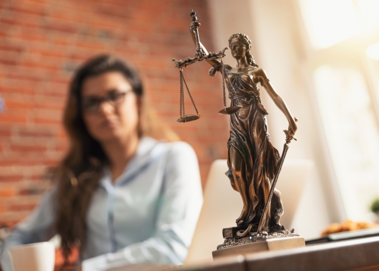 Fru justitia staty i förgrunden med en propert klädd ung kvinna i bakgrunden