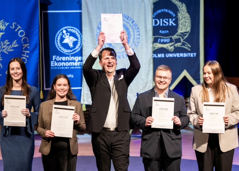 Five persons standing in a row showing their diplomas.