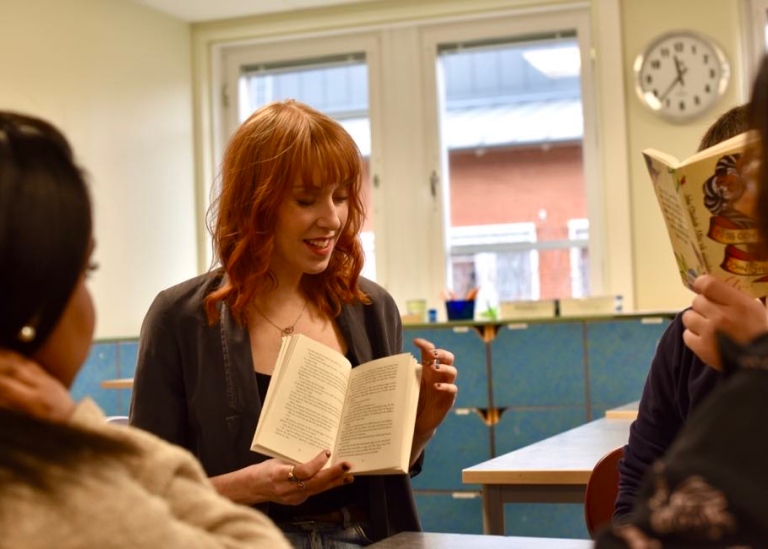Malin står framför eleverna och pekar i en bok som hon håller i