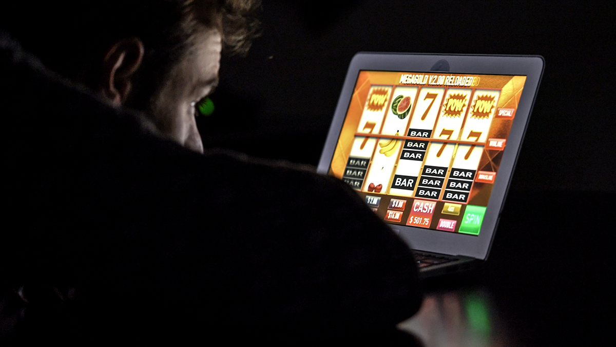 Man with glasses in front of online casino slot machine on laptop computer at night