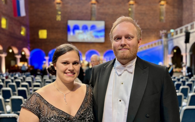 En kvinna och en man står festklädda bredvid varandra i Stockholms stadshus.
