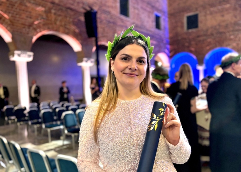 Festklädd kvinna med en lagerkrans på huvudet. I handen håller hon sitt doktorsdiplom.