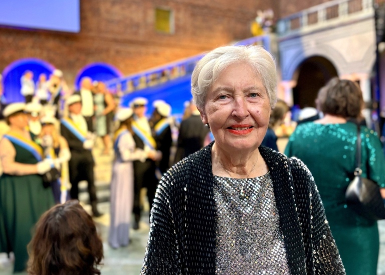 Kvinna i silvrig paljettklänning. I bakgrunden skymtar festklädda marskalkar i studentmössor.