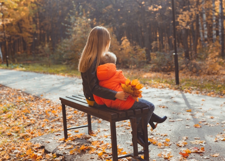 Singelmamma med ett barn på en parkbänk, höstväder