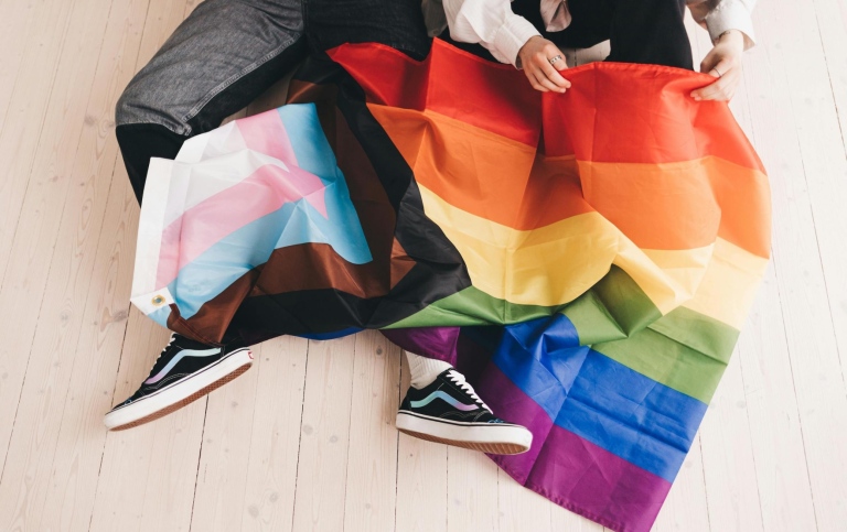 Två personer som vecklar ut en LGBTQIA+ flagga. Foto från Pexels