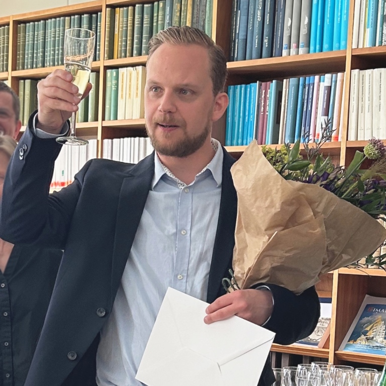 En person står med ett glas och skålar med en blombukett i hand.