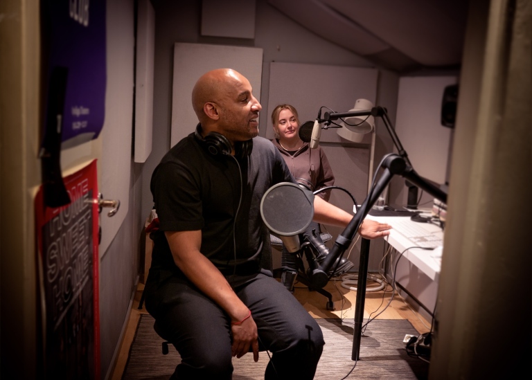 Två personer framför var sin mikrofon i en liten studio.