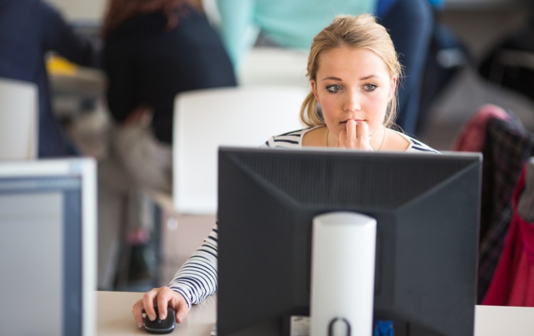 Ung kvinnlig student framför datorskärm, fundersam.