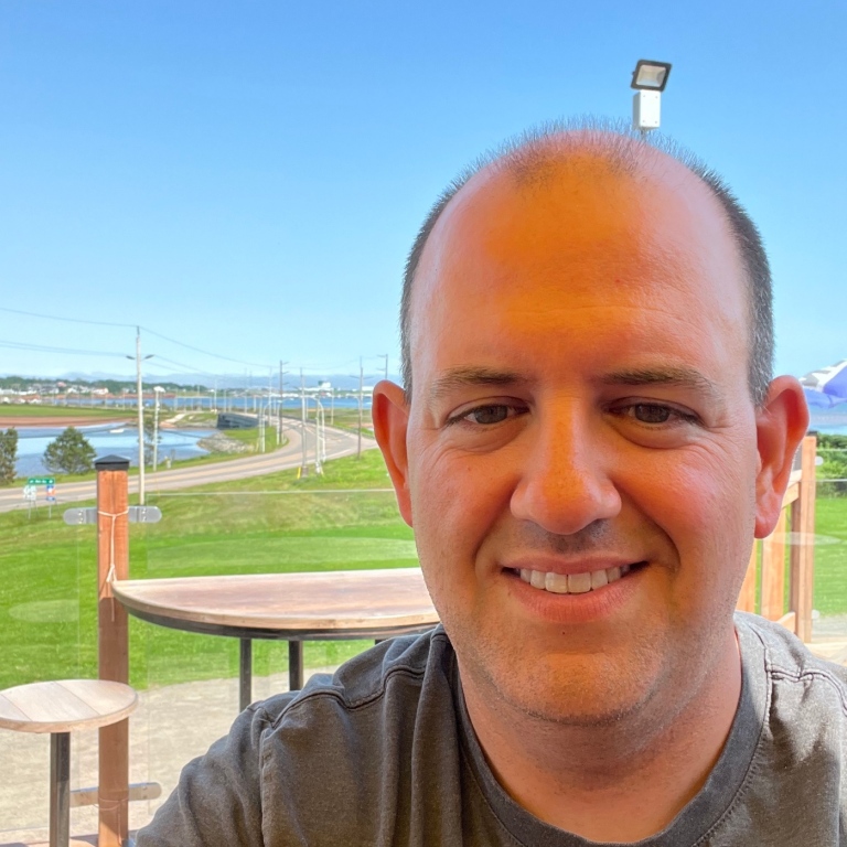 Evan O'Connor smiling in front of a green field and blue sky.