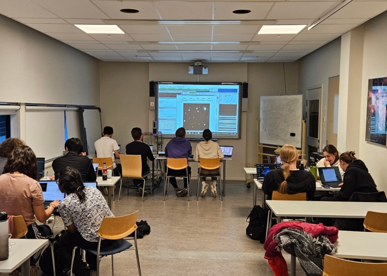 Students in a classroom facing a big screen showing telescope controls