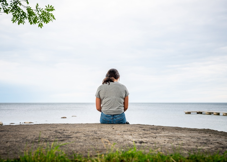 Ensam flicka sitter på en klippa och tittar på havet