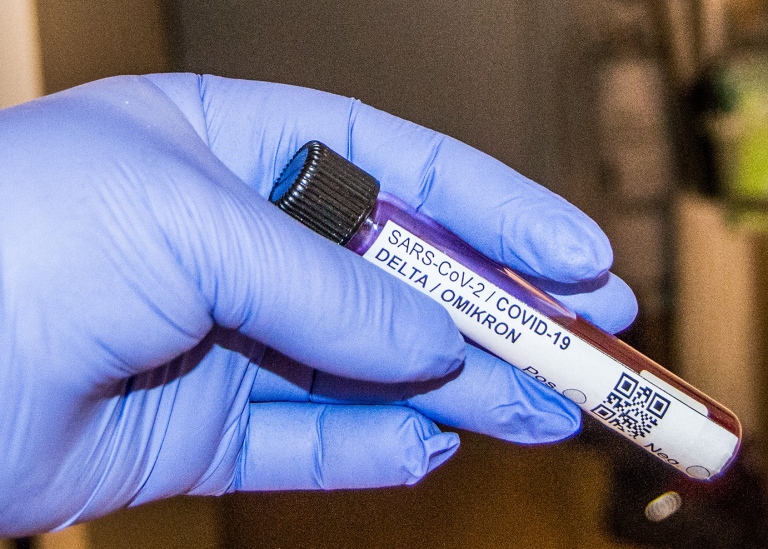 A hand with a blue glove holding a test tube with a Delta / Omikron COVID19-test.