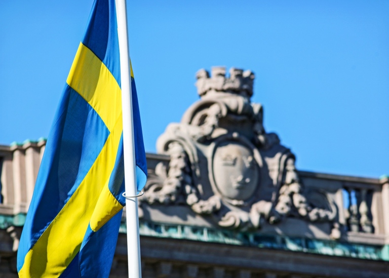 Detaljbild på riksdagshuset med sverigeflagga i förgrunden
