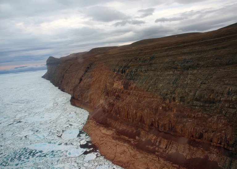 view of geological coast with icebergs and sea ice, dramatic clouds