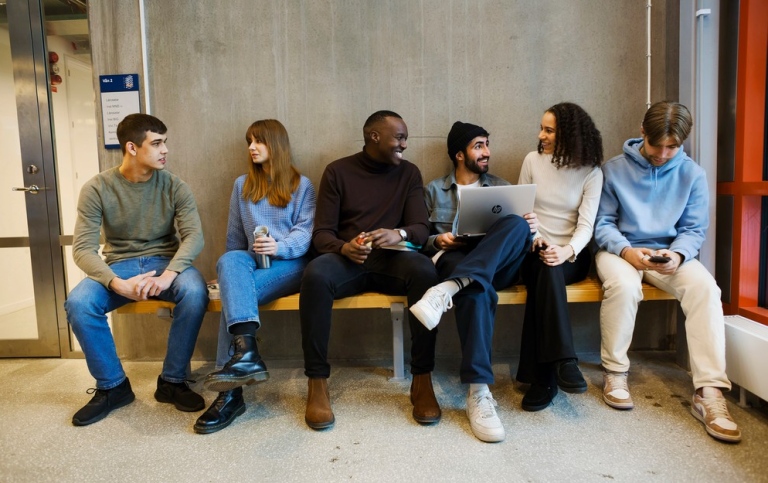 A group of students sitting on a bench indoors, chatting.