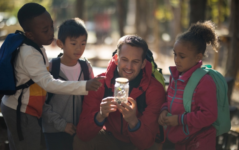 Teacher and kids examining plant in a jar.