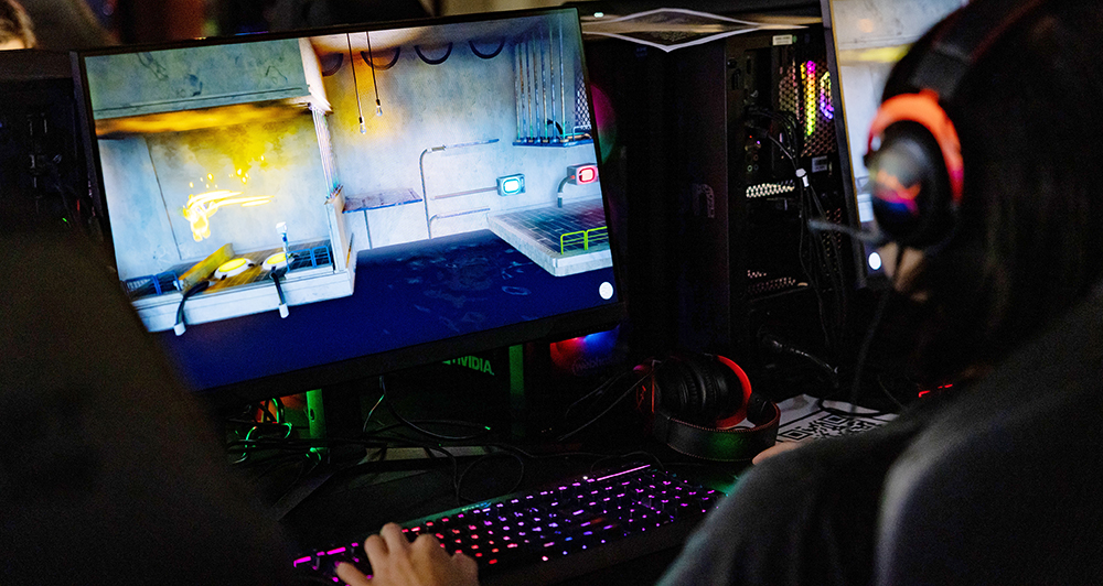 A person in head phones with neon effect ligheting on is playing a computer game. 