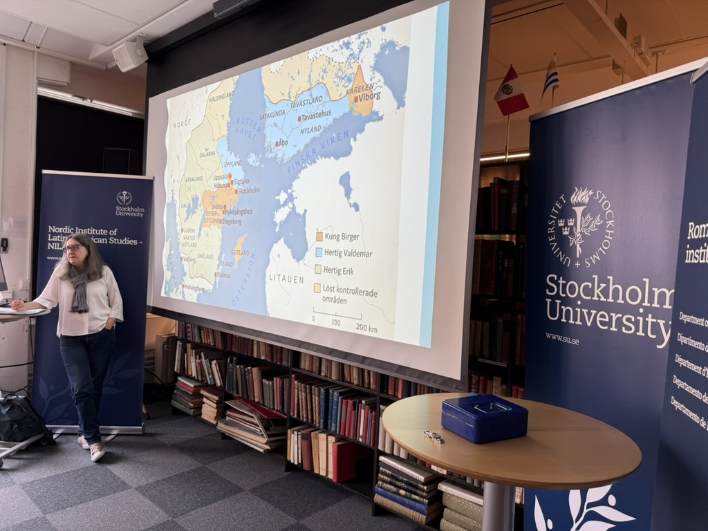En person håller en presentation vid Nordiska Latinamerikainstitutet (Stockholms universitet) framför en projicerad historisk karta över Sverige och Finland. På kartan markeras områden kopplade till bland andra Kung Birger, Hertig Valdemar och Hertig Erik.