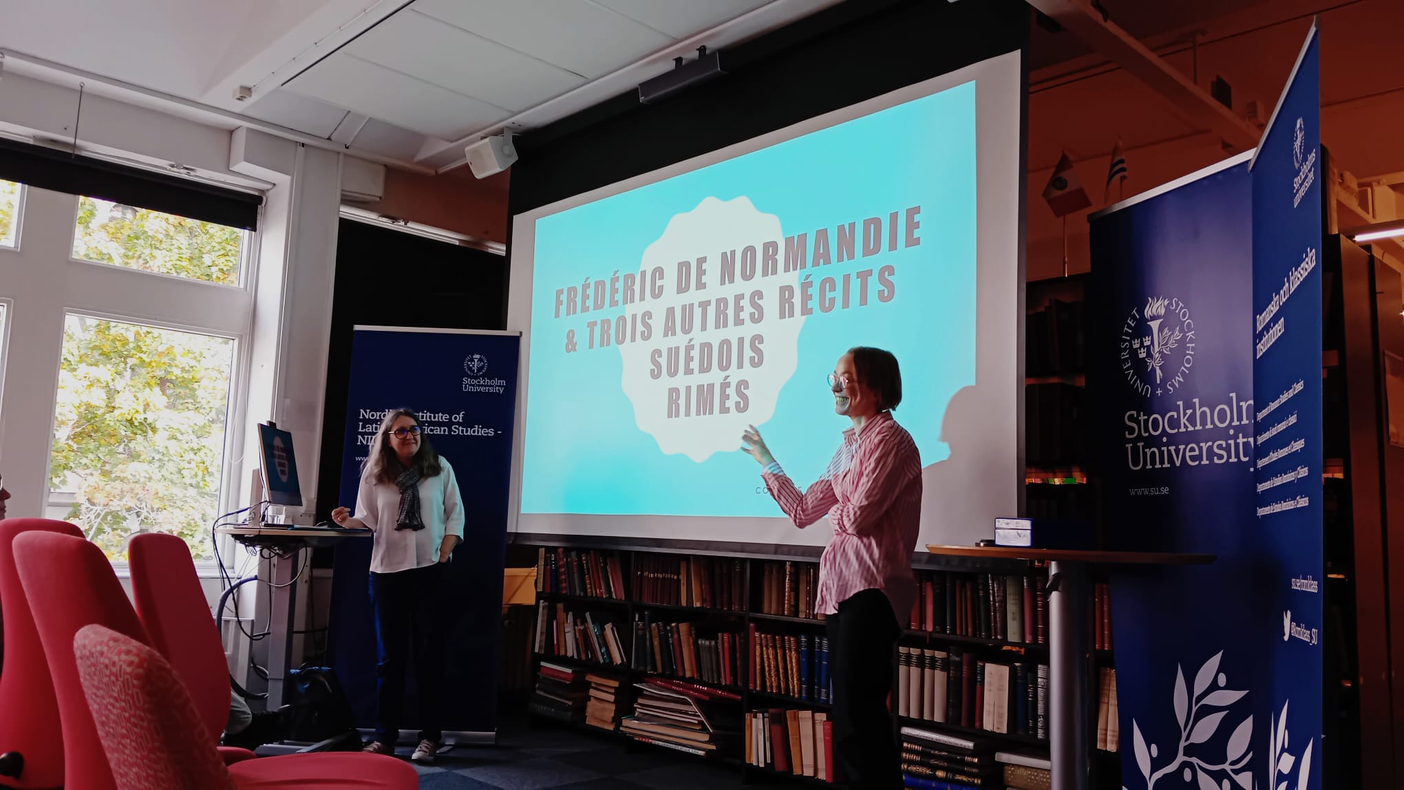 Två personer står framför en presentationsskärm vid Nordiskalatinamerikainstitutets bibliotek (Romklass/Stockholms universitet). På skärmen står den franska rubriken ”FRÉDÉRIC DE NORMANDIE & TROIS AUTRES RÉCITS SUÉDOIS RIMÉS.