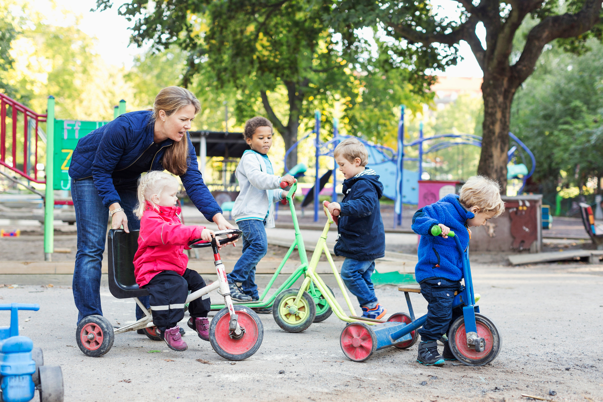 Förskolebarn är utomhus och cyklar på trehjulingar tillsammans med en pedagog.
