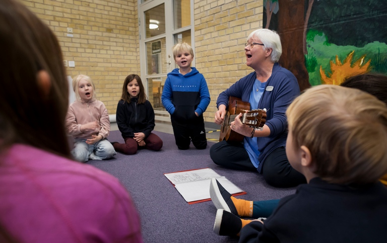 Lärare spelar gitarr och sjunger tillsammans med barn i förskoleklass.