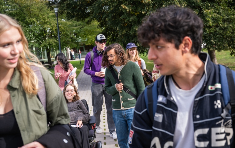 En grupp studenter går och åker permobil utomhus och pratar.
