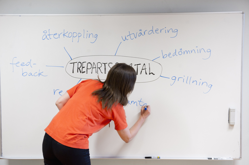Lärare skriver om trepartssamtal på en whiteboardtavla.