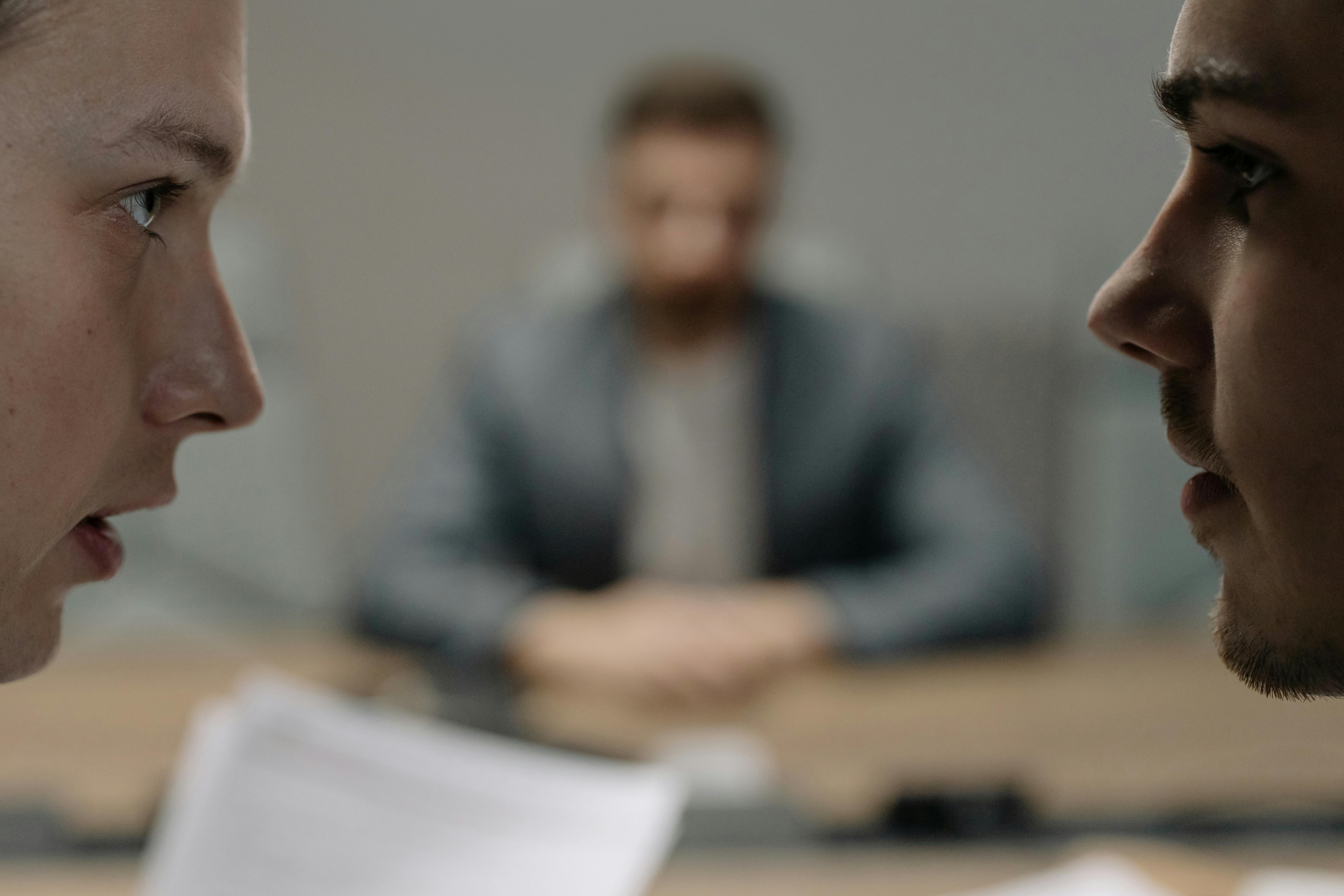 Närbild på två personer som tittar på varandra, med en tredje suddig person i bakgrunden.