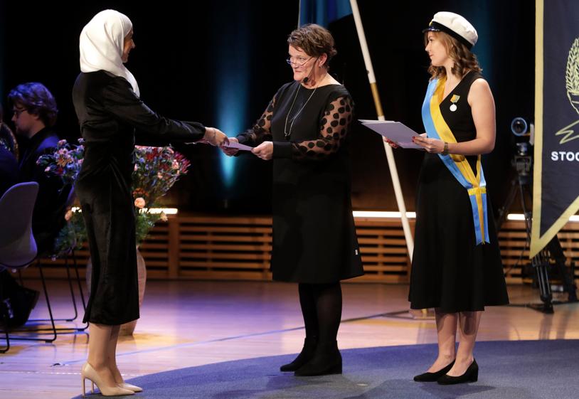 En kvinna tar emot diplom från en annan kvinna. Ytterligare en kvinna står bredvid med ett diplom i handen.
