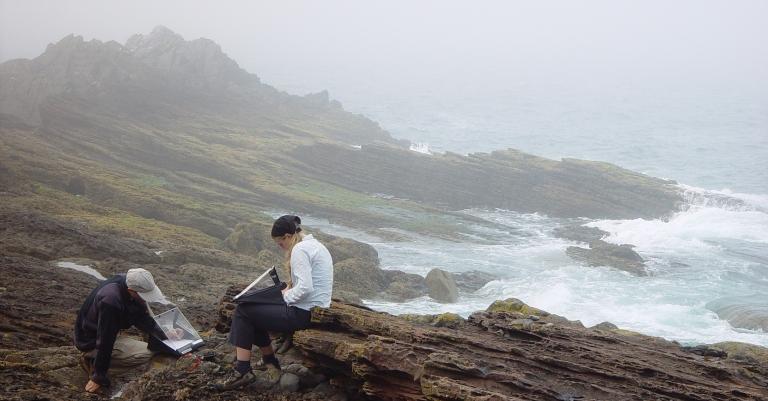 students sitting on a bedrock by the ocean writting notes