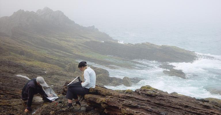 students sitting on a bedrock by the ocean writting notes
