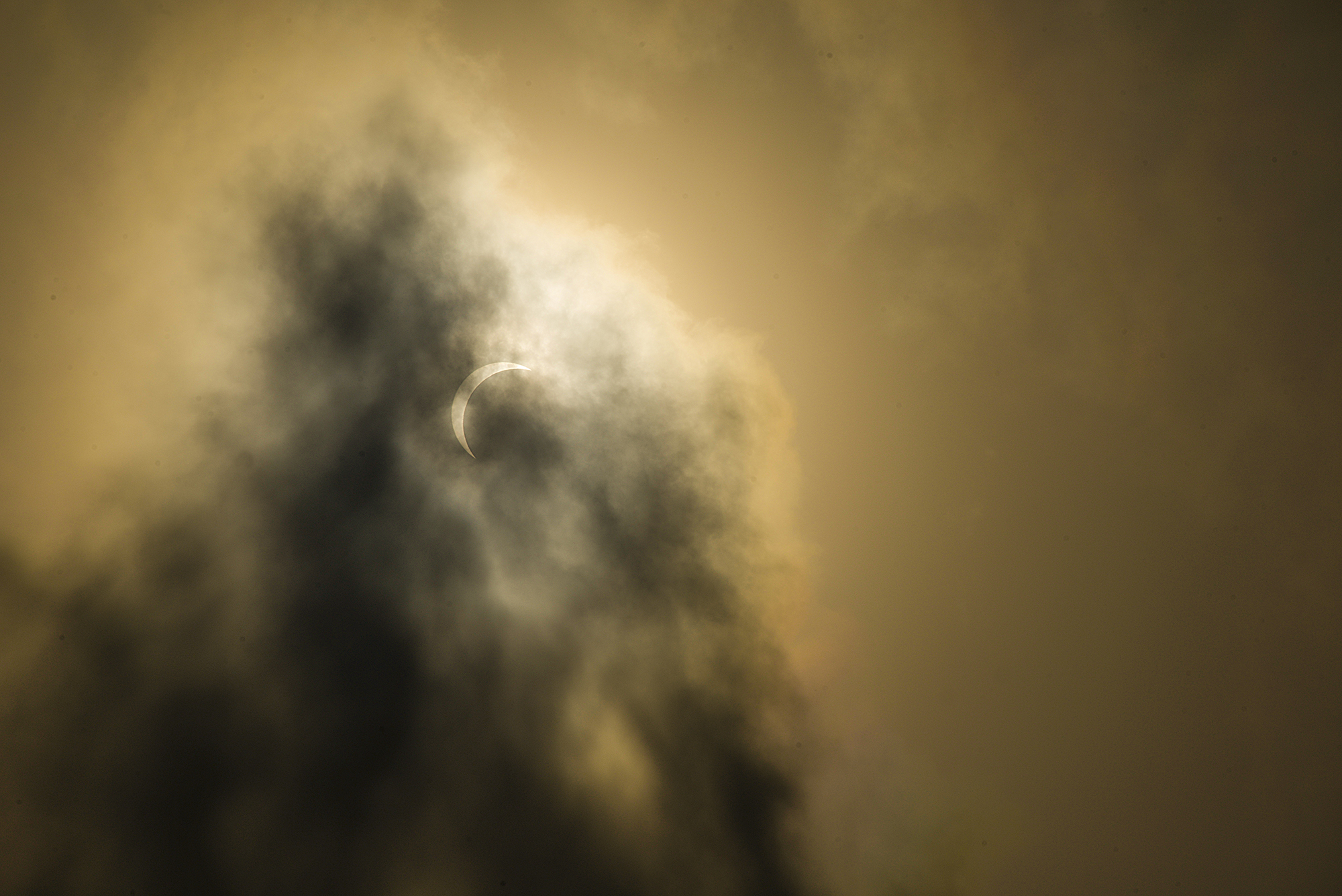 Solförmörkelse med molnslöjor mot gul himmel