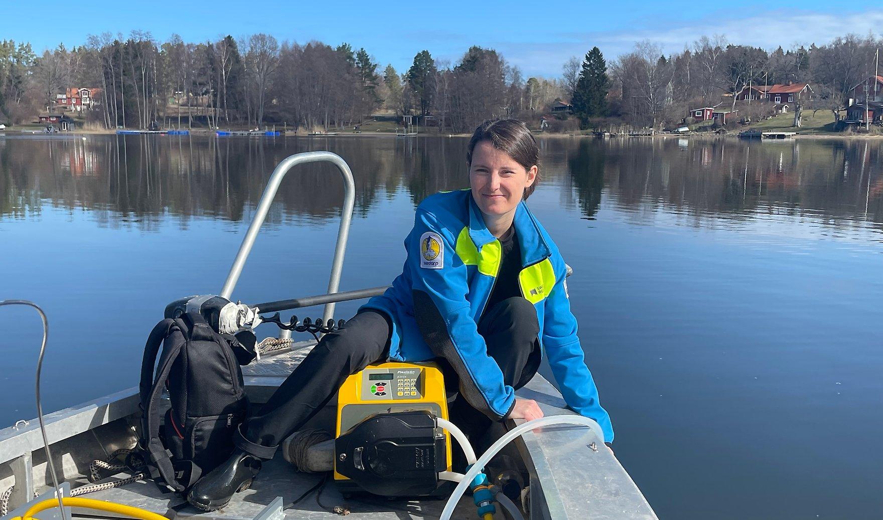 Researcher standing on a small boat on a calm lake in Sweden, holding equipment over the water while conducting fieldwork.
